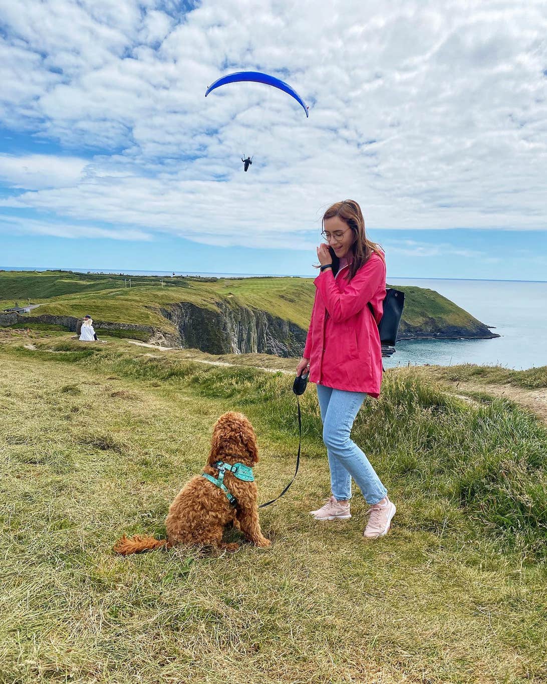 A womand and her dog enjoy the scilly cliff walk in Kinsale, with a paraglider in the background.