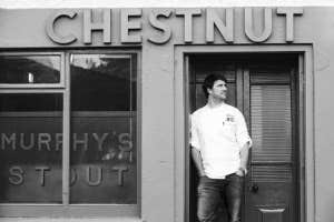 Black and white image of the exterior of the restaurant with the chef standing in the doorway