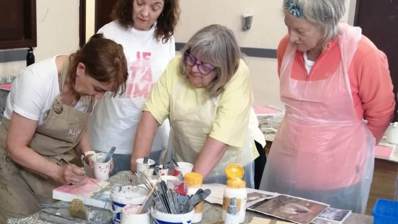 People in protective aprons and a teacher gathered around a table with art supplies