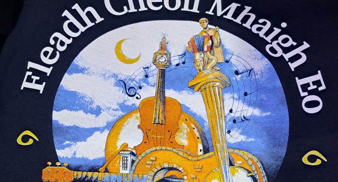 ​Fleadh Cheoil Mhaigh Eo. Circular logo including string instruments on water with blue sky.