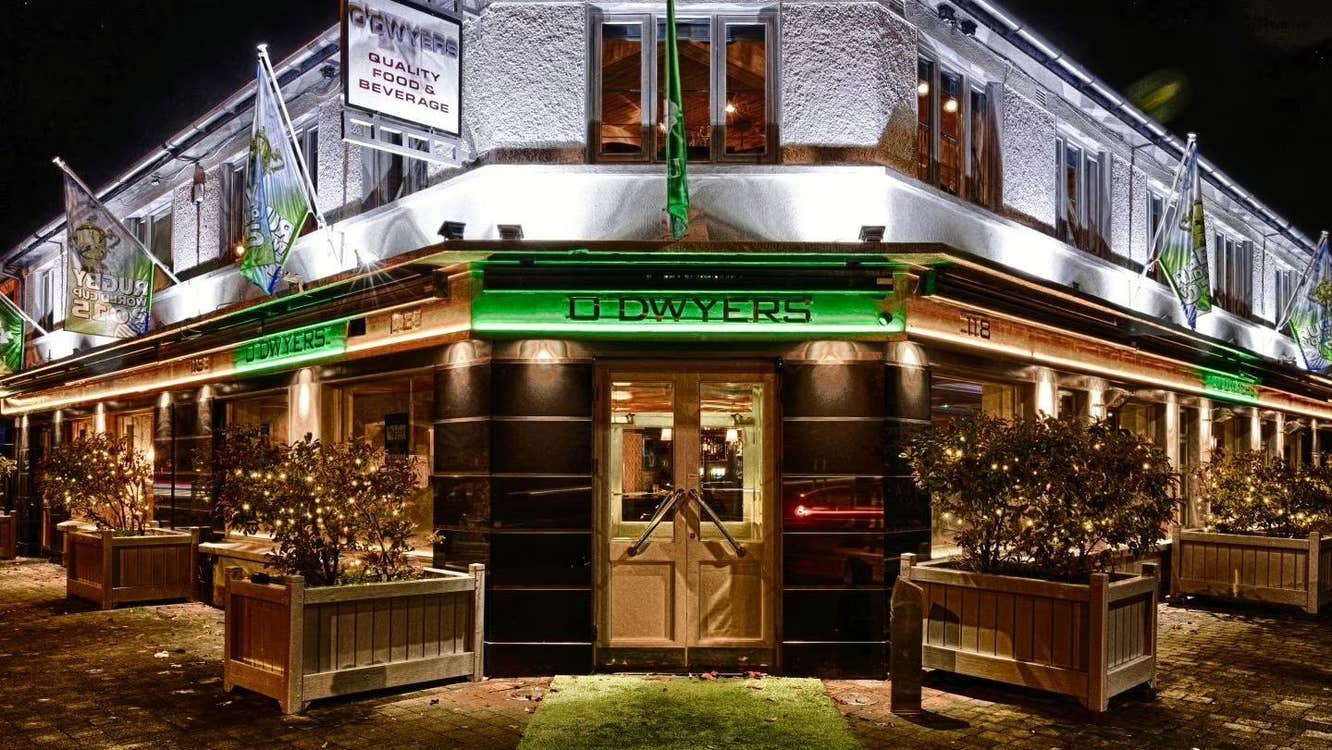 Outside a pub on a corner at night with the name on a green background and planters either side
