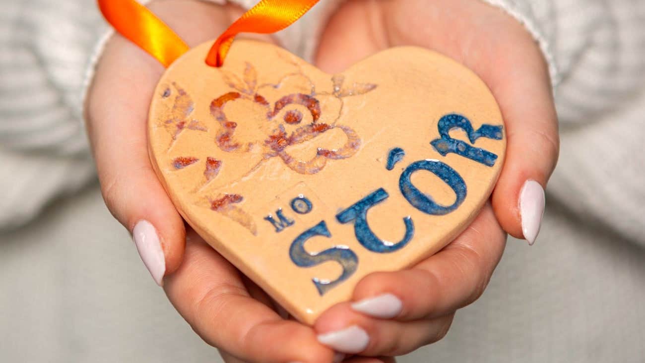 A lady's hands holding a clay heart engraved with Irish text
