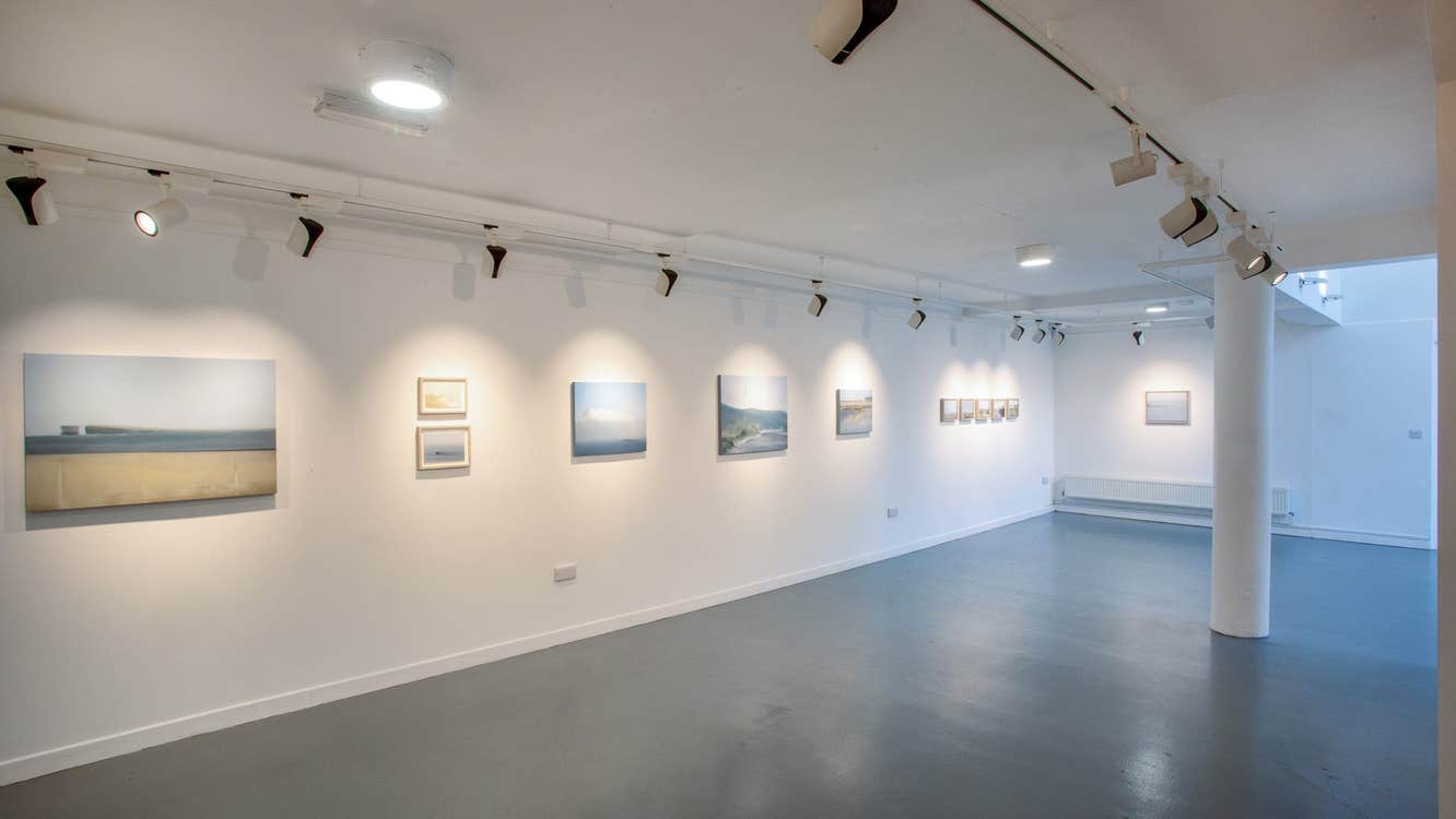 Gallery with dark wooden floors a white column and white walls with art displayed on them