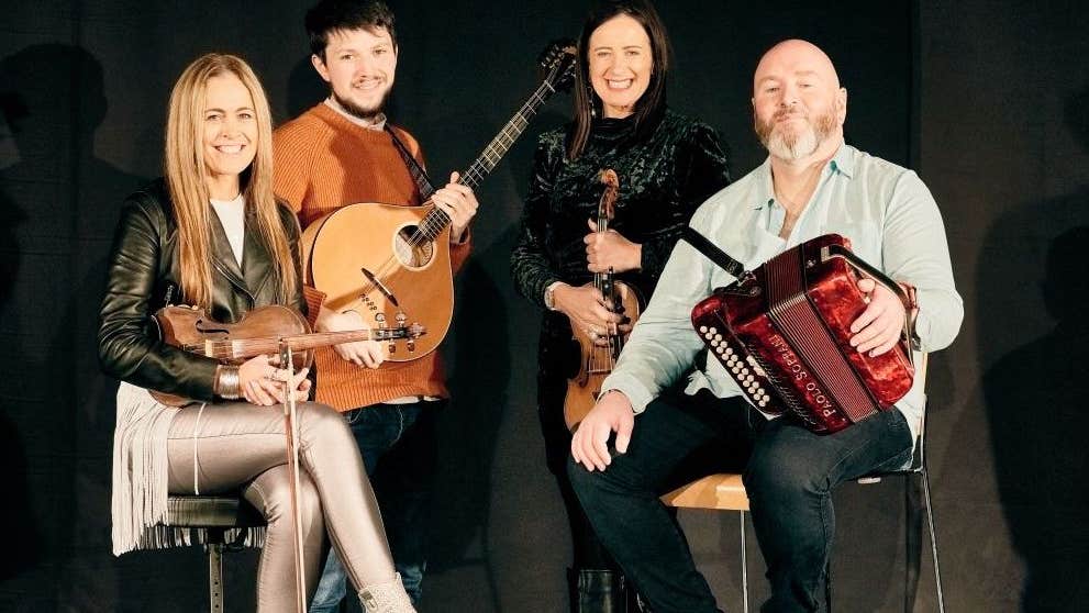 Derek Hickey, Liz & Yvonne Kane and Macdara Ó Faoláin are on a stage with traditional Irish instruments.