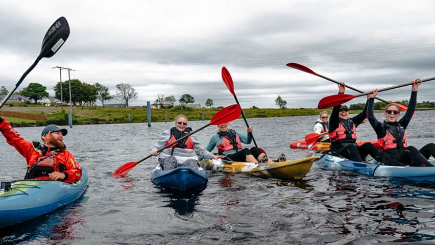 A group of six kayakers holding their paddles over their heads