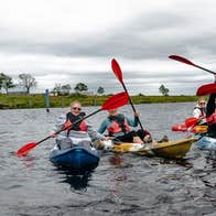 A group of six kayakers holding their paddles over their heads