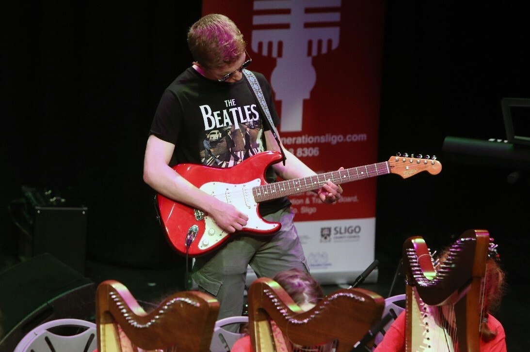 A person in black tshirt is playing a red and white electric guitar.