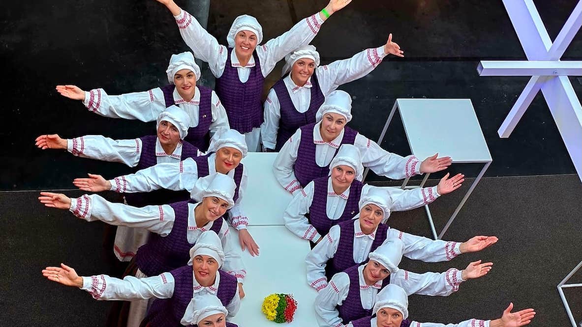 Suktinis Lithuanian folk dance group standing around a table with their arms outstretched.