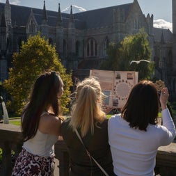 Three girls looking at a map standing by a wall with a church in the background