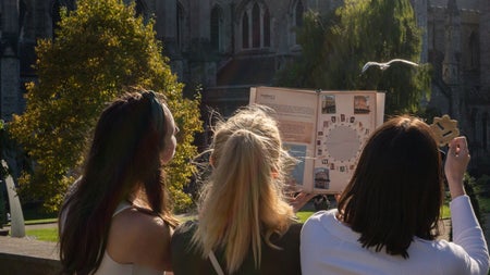 Three girls looking at a map standing by a wall with a church in the background