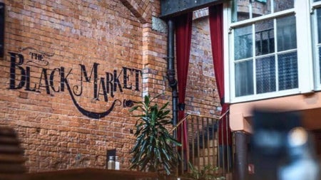 Exposed brick wall with The Black Market sign red velvet curtains and a staircase leading to an upper level