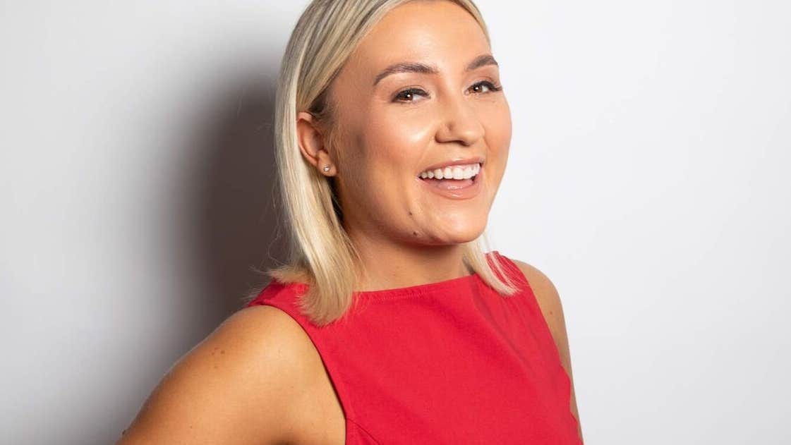 Enya Martin, a smiling woman in a red dress against a plain, light background.