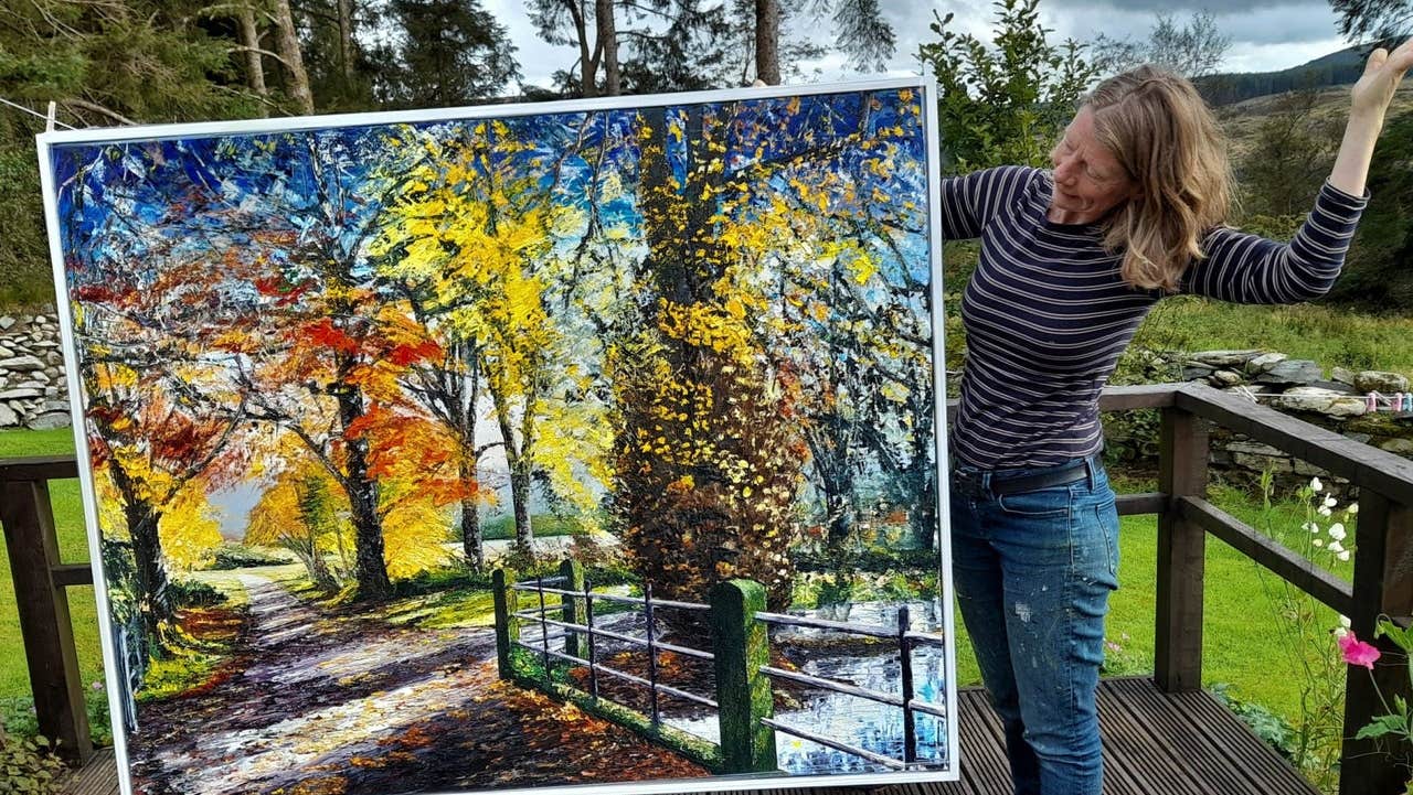 An artist standing outside displaying her oil painting