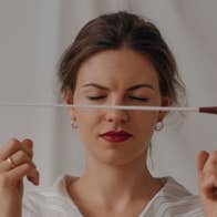 A woman with closed eyes is holding up a baton in front of her face between two index fingers