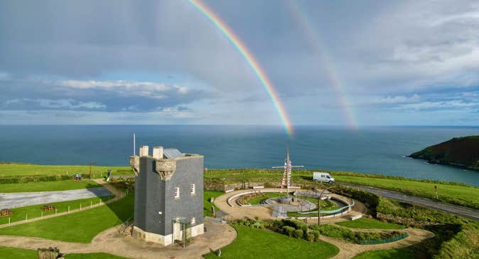 A signal tower beside the coast with a double rainbow in the sky