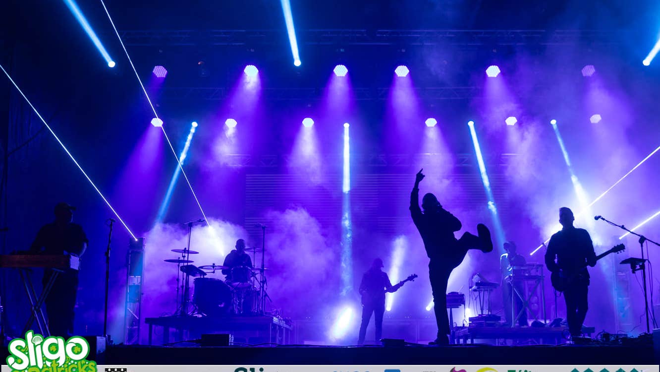 A stage with white spotlights and performers in silhouette.