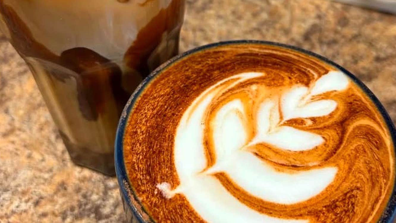 A coffee with a milk froth design on top and a glass of ice coffee served at Panama Café