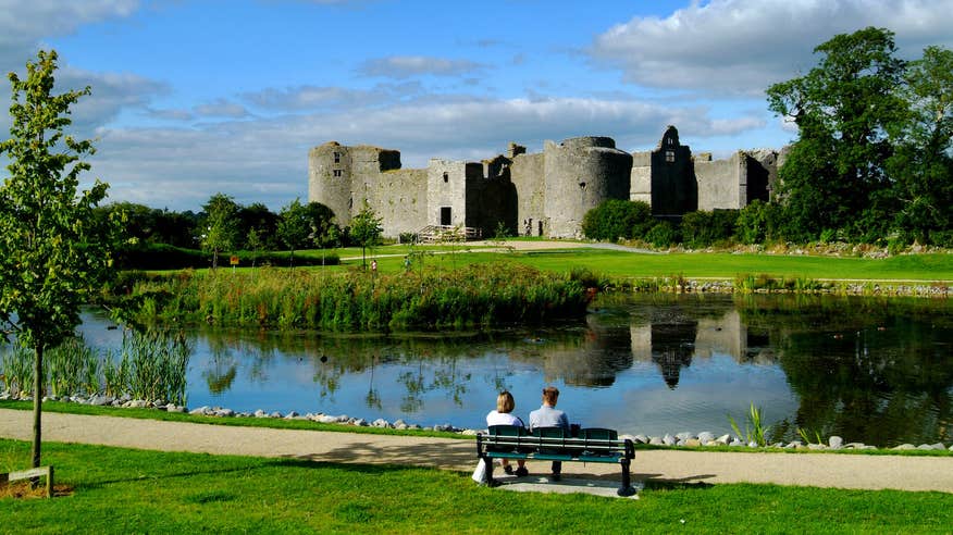 Two people sitting on a bench looking across the river at Roscommon Castle in County Roscommon