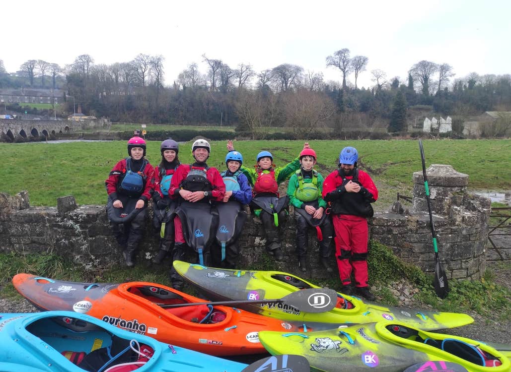 A group of young people by a stone wall with colourful kayaks in front of them
