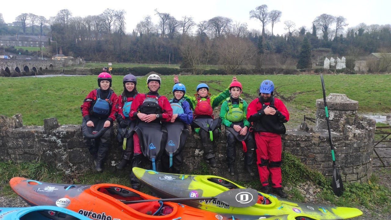 A group of young people by a stone wall with colourful kayaks in front of them