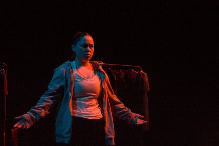 On a dark stage a person is standing with their arms out wide, lit in red.