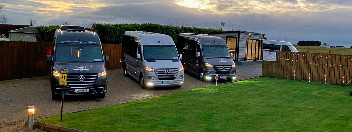 Three Mercedes class mini buses parked together at dusk with their lights on