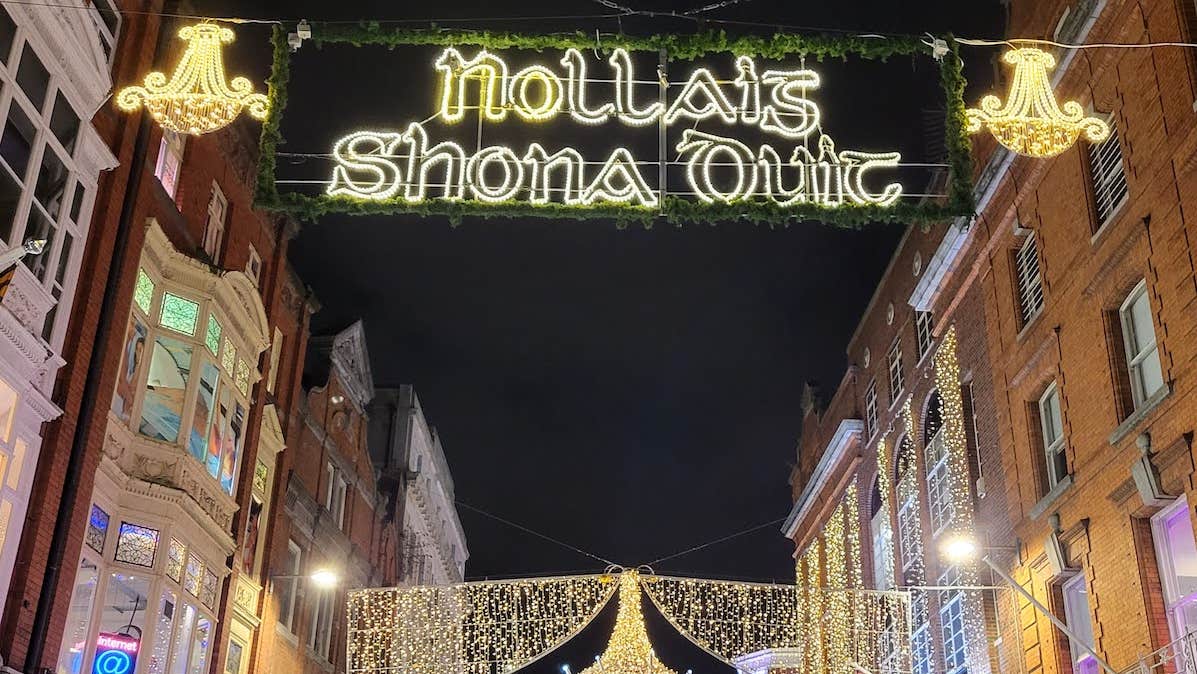 Looking up at buildings in a street at night with yellow christmas lights across the between them.