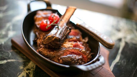 A small pan with a steak garnished with some herbs and tomatoes