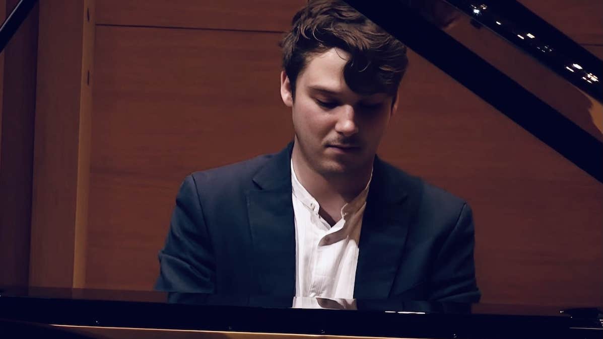 A man looking down at keyboard, seated at a grand piano