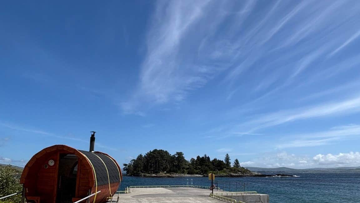 Mobile sauna unit on a pier with an island close by and blue skies overhead