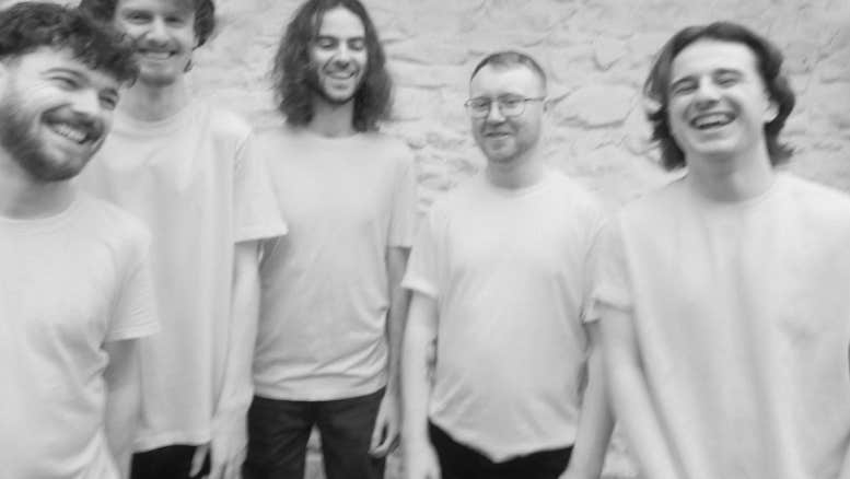 Pale, slightly blurry photo of 5 happy looking men in plain Tshirts