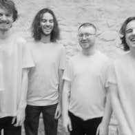 Pale, slightly blurry photo of 5 happy looking men in plain Tshirts