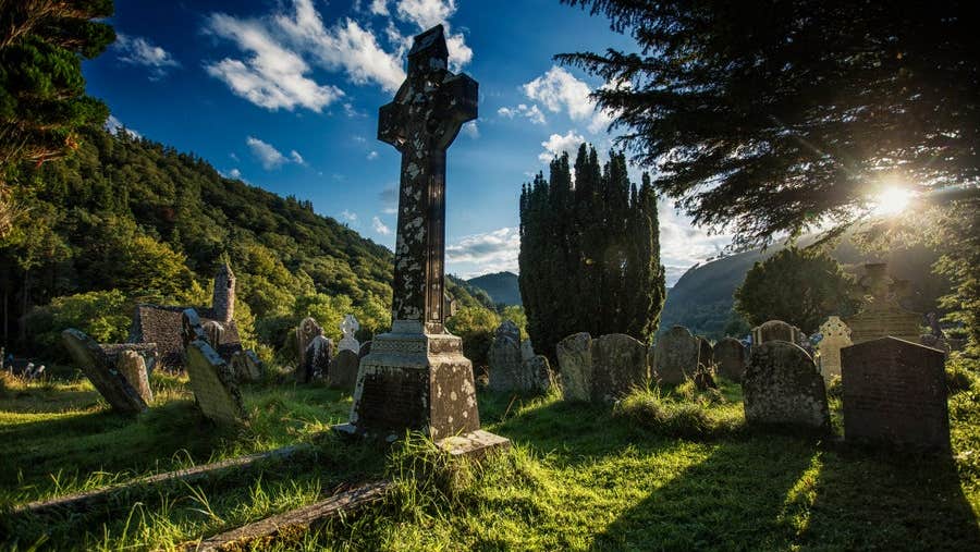 A stone high cross in a grassy cemetery under a blue sky