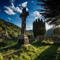 A stone high cross in a grassy cemetery under a blue sky