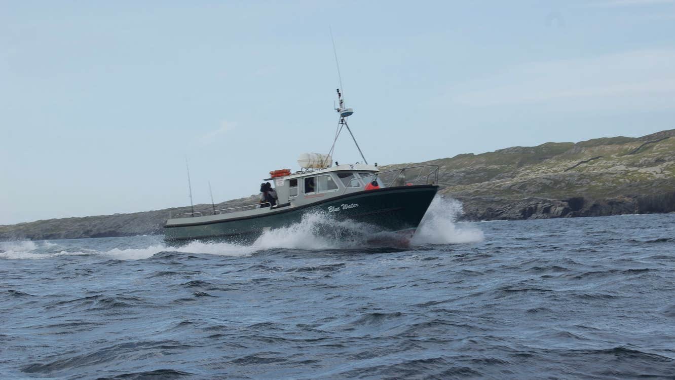 Fishing trawler at sea in rough waters with green hills to the right