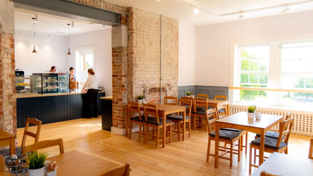 Bright café interior with wooden tables, exposed brick and a counter with staff serving customers