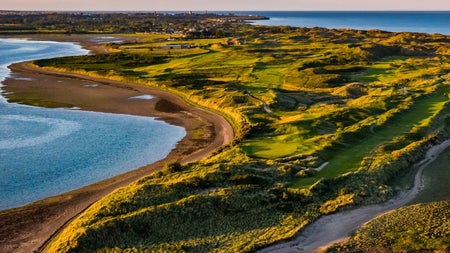 Aerial view of golf course surrounded on either side by the sea and a beach on the left