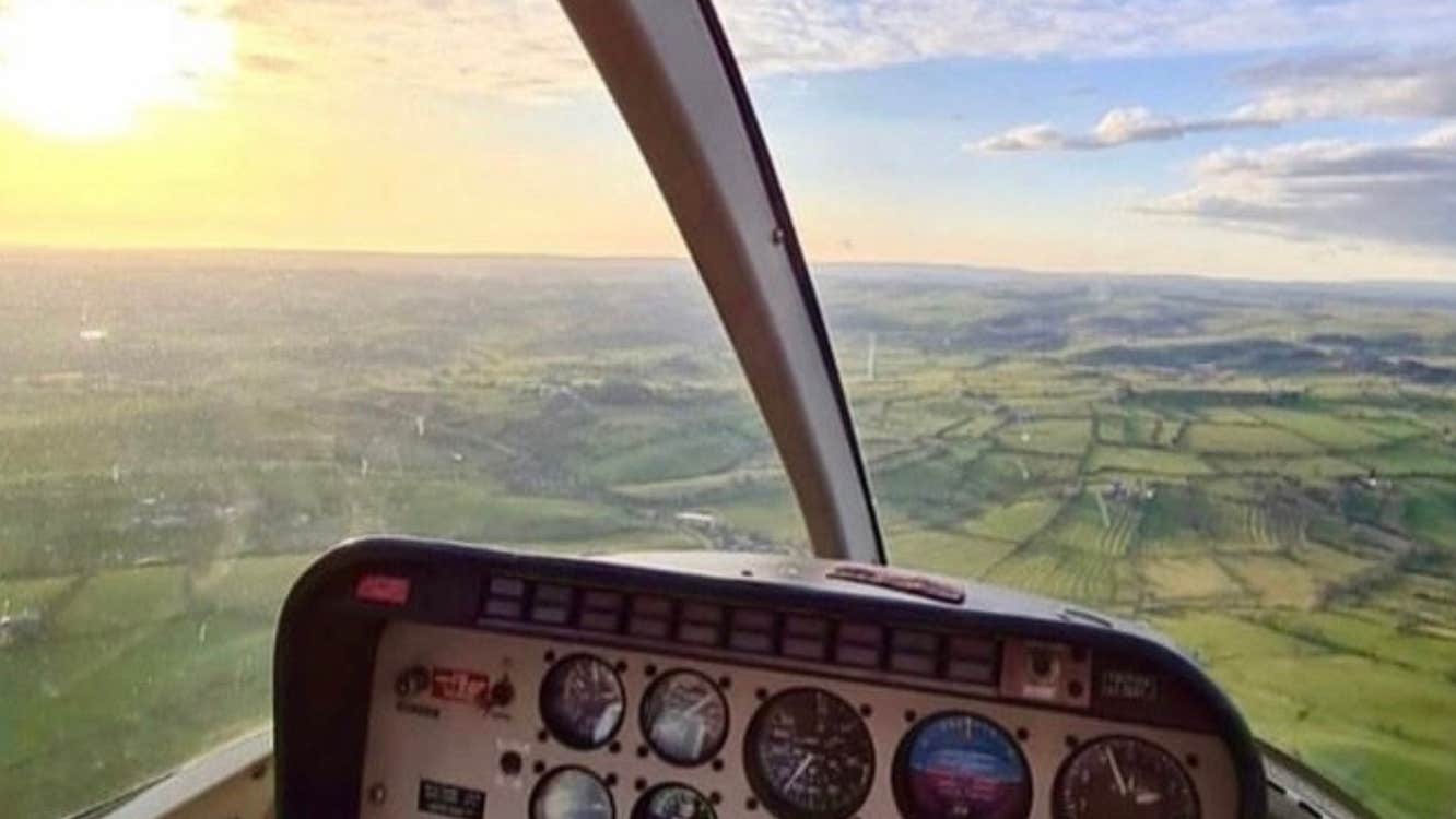 An aerial image captured inside the helicopter of the green landscape below with the sun shining