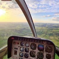 An aerial image captured inside the helicopter of the green landscape below with the sun shining