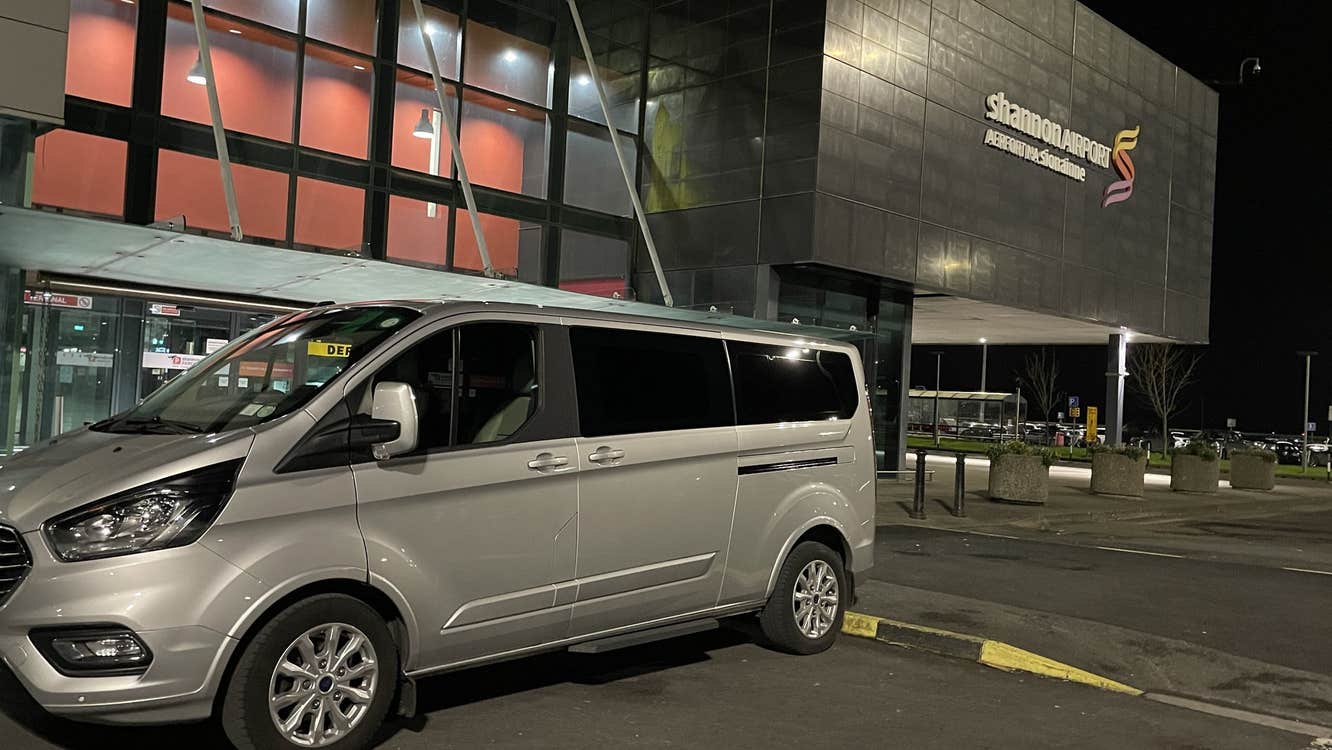Silver mini bus parked outside an airport at night
