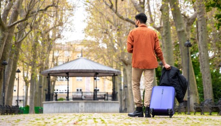 A man standing with a suitcase and jacket in a city park