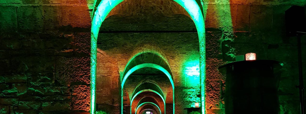 View down a large, vaulted, brick corridor lit with red and mostly green lights.