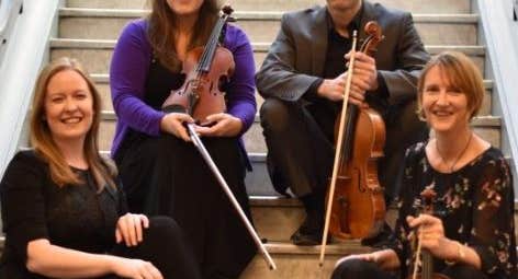 4 smiling people are seated on stone stairs each holding string instruments
