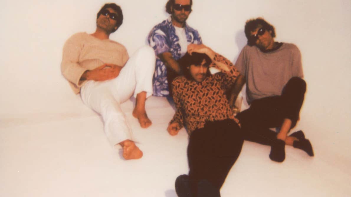 Slightly blurry photo of 4 men lounging on an off white floor and wall.