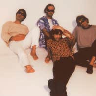Slightly blurry photo of 4 men lounging on an off white floor and wall.