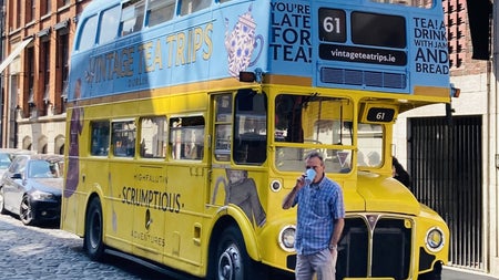 Parked blue and yellow bus with a man drinking from a takeaway cup standing in front