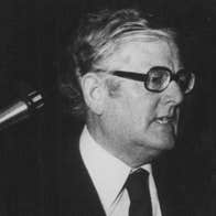 Old black and white, slightly grainy photo of man in suit and tie giving a speech