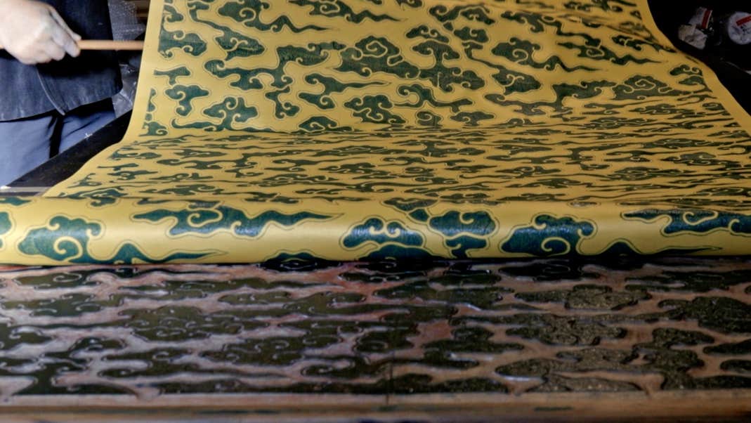 A long strip of patterned paper being rolled up from the print blocks