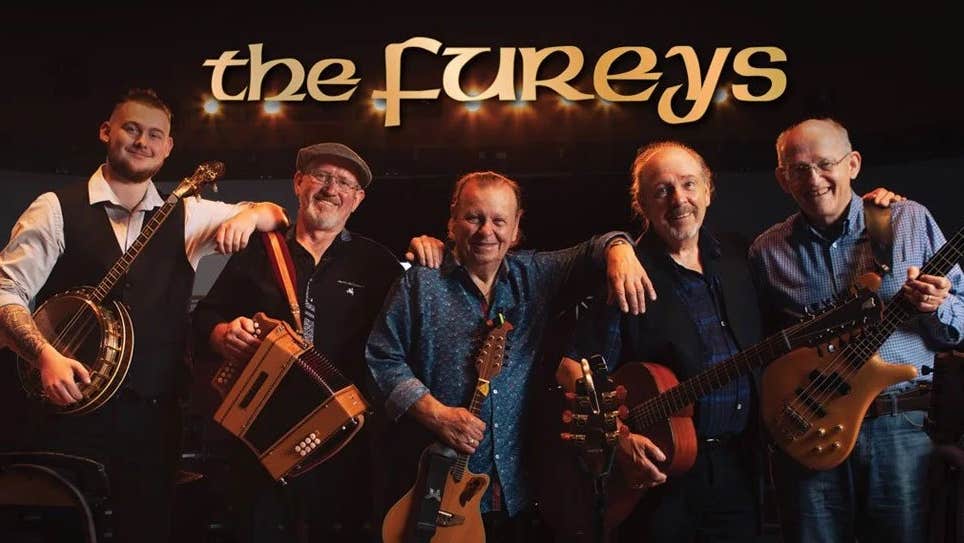 A line of 5 smiling older men with musical instruments