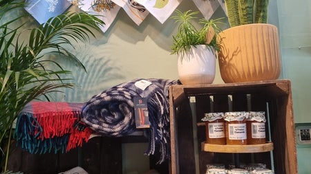 A selection of coloured handmade throws and scarves on display with homemade jars of chutney and jams